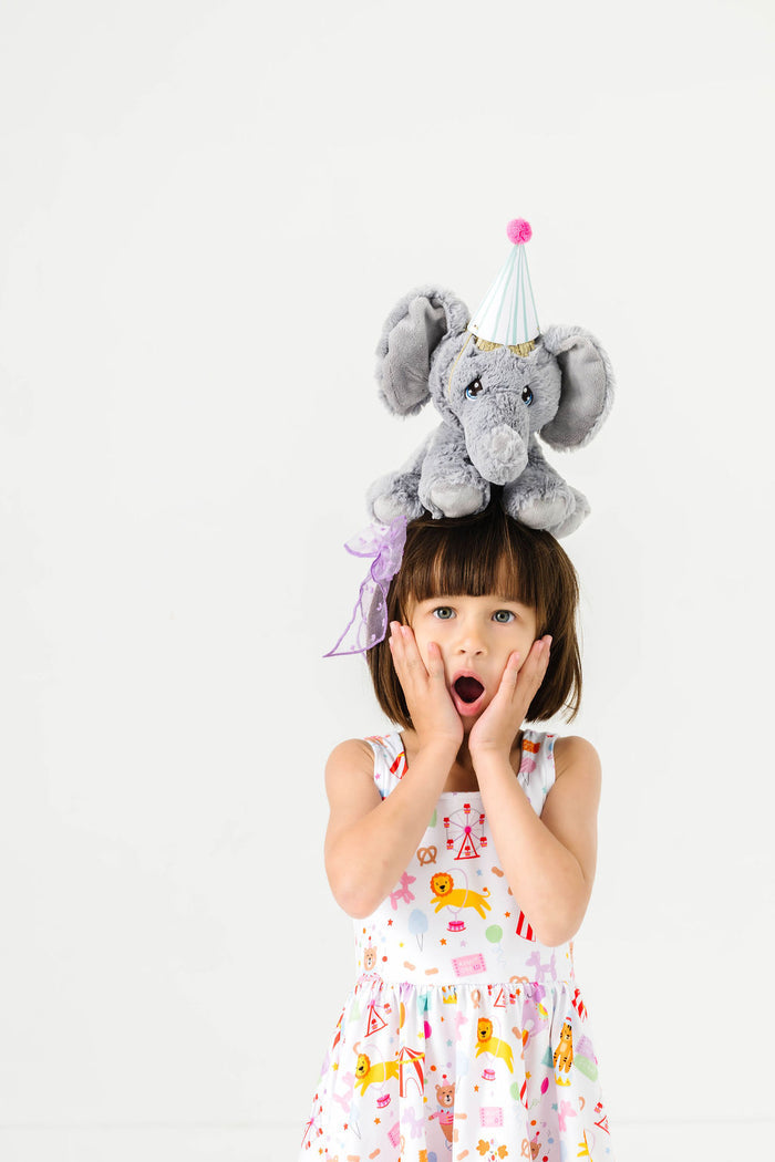 little girl with stuffed elephant on her head wearing sleeveless circus print twirl dress