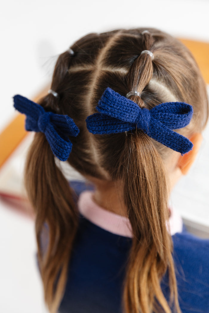 little girl in navy yarn pigtail bows and matching navy girlhood sweater