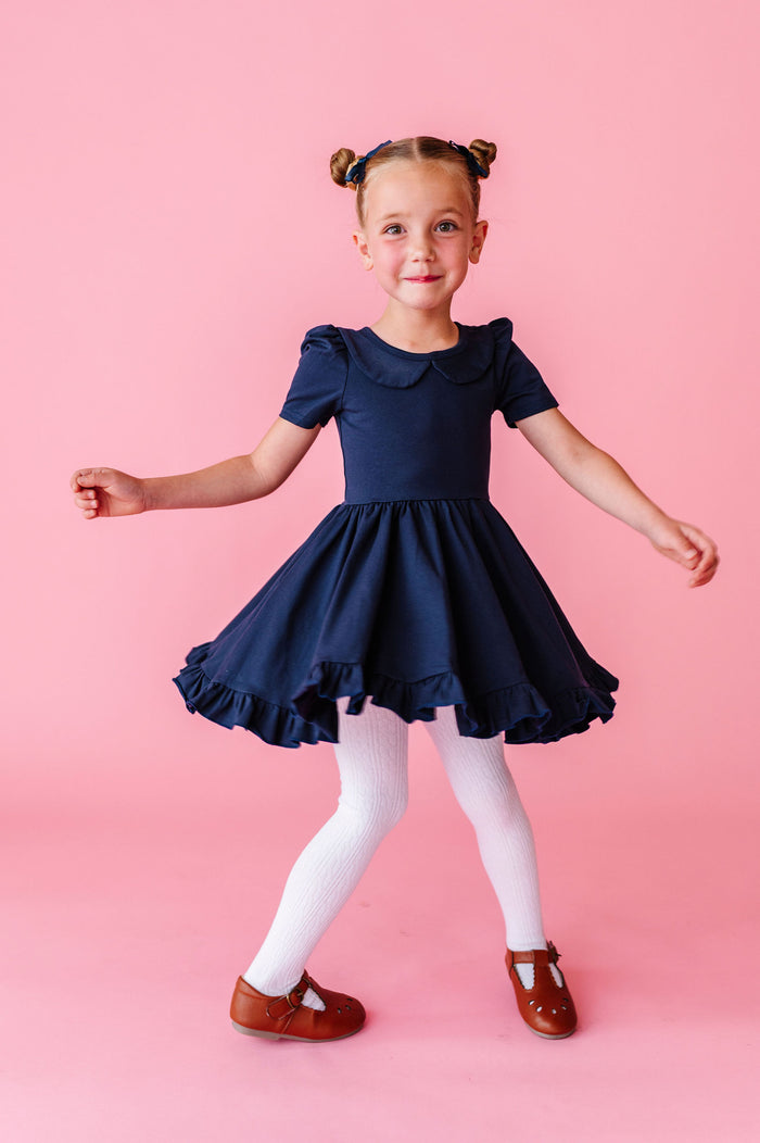 girl twirling in navy cotton dress with collar and white cable knit tights