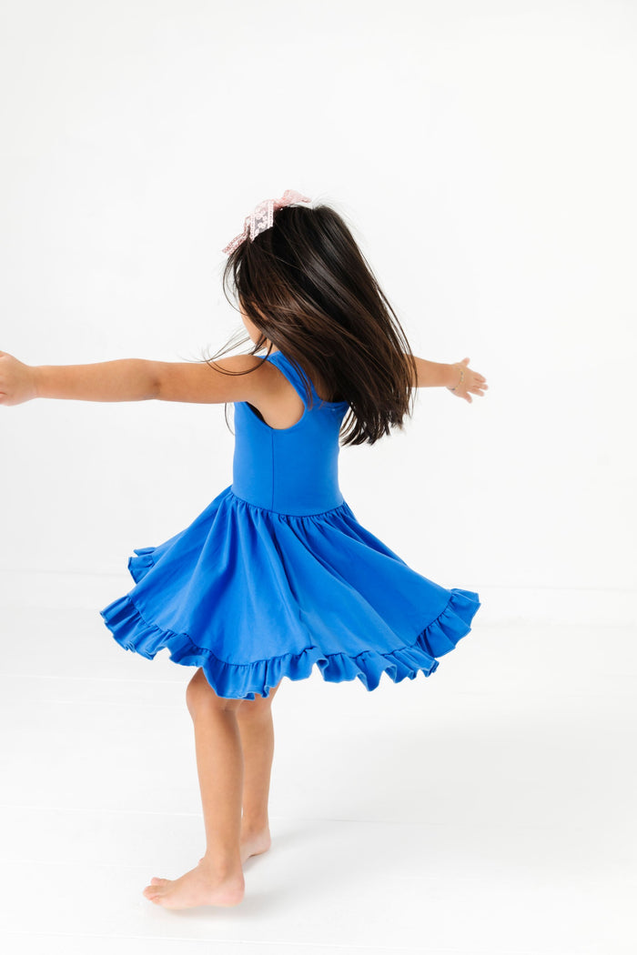 young girl twirling in sleeveless bright blue twirl dress and light pink lace hair bow