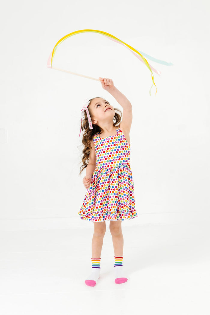 little girl with streamers in sleeveless twirl dress with a rainbow of small retro flowers paired with matching rainbow striped crew socks