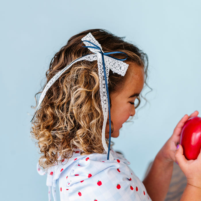 girl holding apple in white lace long tail hair bow on clip with navy satin ribbon detail to match gingham apple school dress