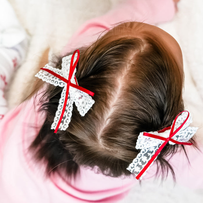 baby girl in pigtail clips with white lace and red ribbon detail
