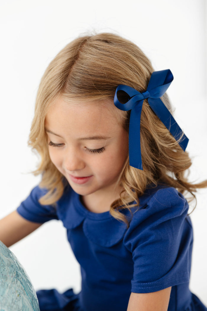 little girl in navy blue collared uniform dress and matching blue satin ribbon bow on clip