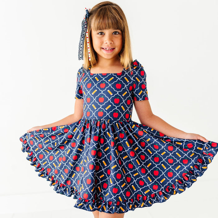 Girl wearing navy back to school dress with apples and pencils