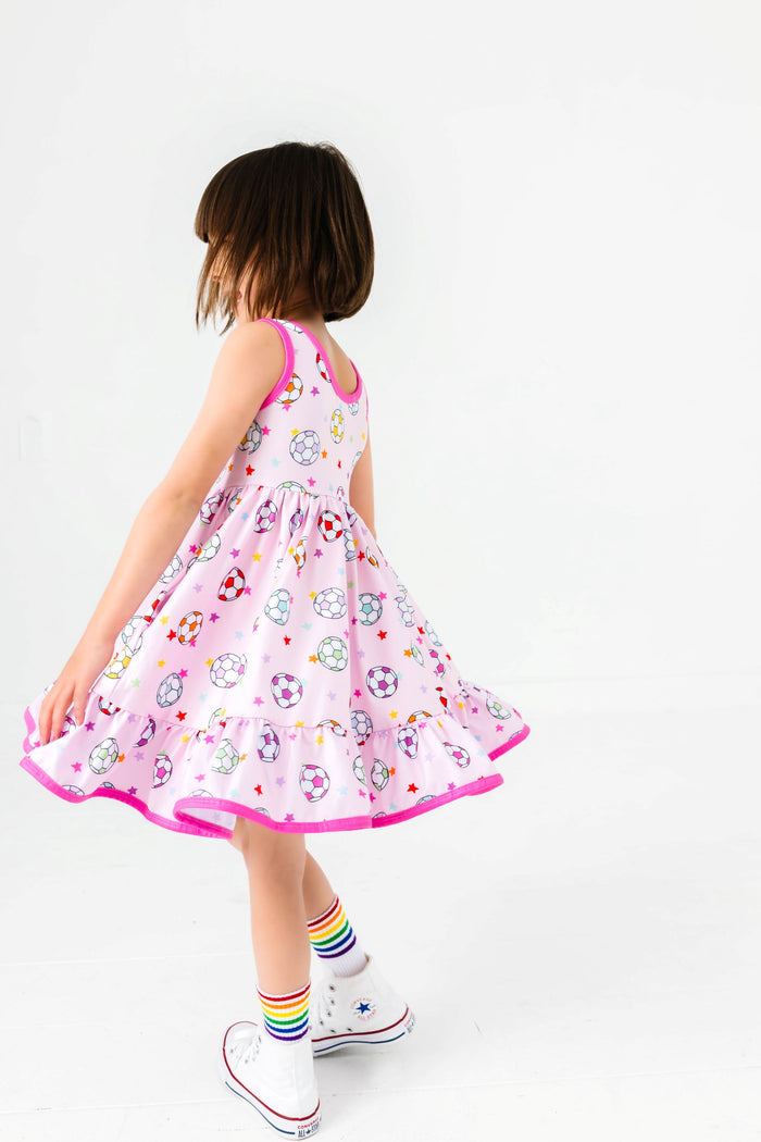 little girl twirling in pink soccer ball print twirl dress with rainbow striped crew socks