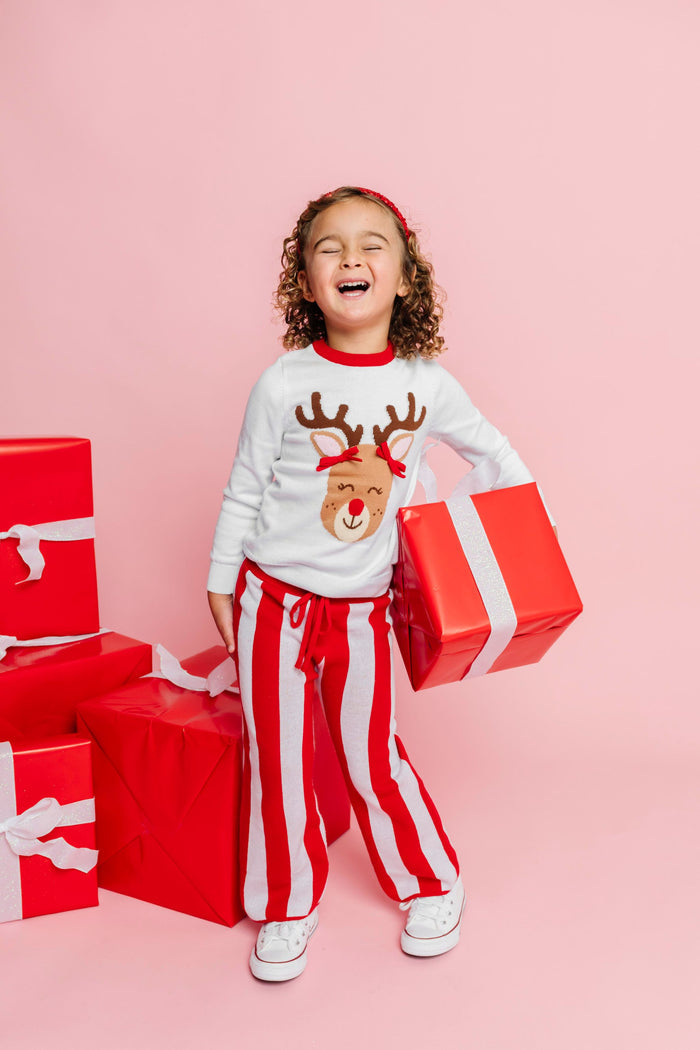 little girl holding Christmas gift in white sweater with Rudolph wearing 3D pigtail bows paired with red and white cotton knit sweater pants