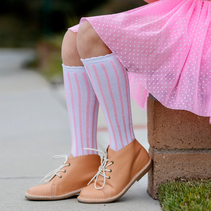 girl sitting with pastel pink tutu skort with white dots paired with white and pink vertical striped knee-high socks with white scalloped trim