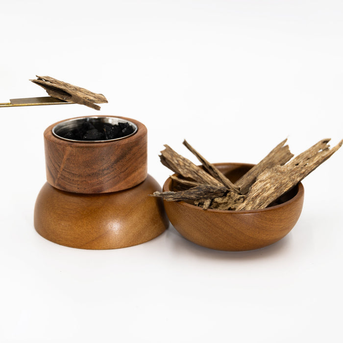 Natural agarwood chips beside a wooden incense heater and metal tongs