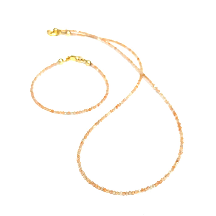 Sunstone necklace detail showing gold-filled clasp and warm peachy-gold round beads with its matching bracelet on a white background, front long view.