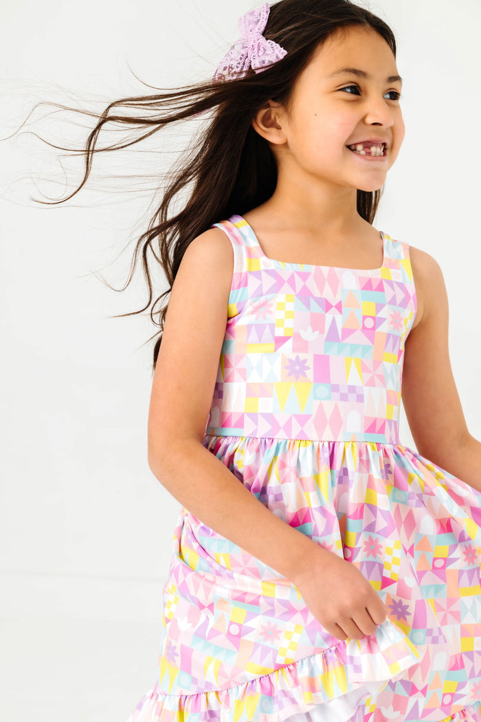 little girl in pastel geometric small world twirl tank dress and lavender lace hair bow