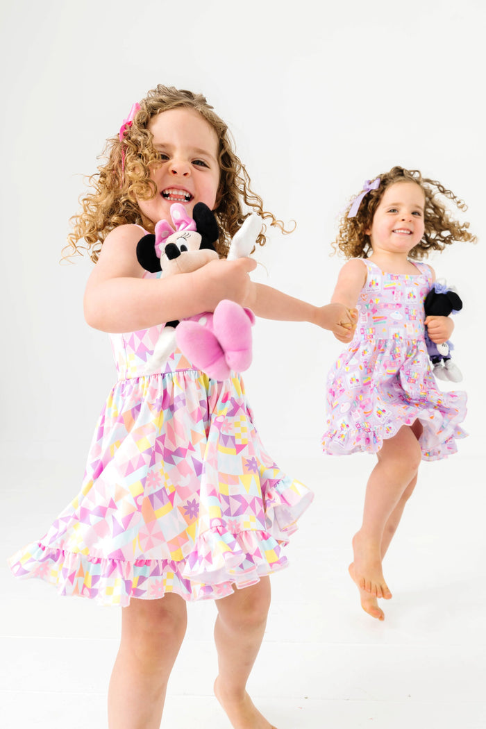 two little girls holding hands and jumping in coordinating theme park inspired twirl dresses and minnie stuffed toys