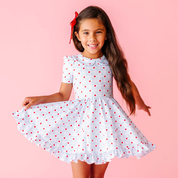 little girl twirling in light blue and white gingham with red apple print short sleeve collared twirl dress