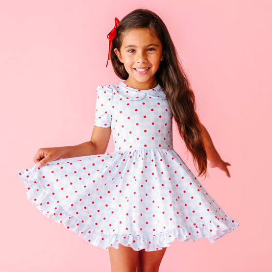 little girl twirling in light blue and white gingham with red apple print short sleeve collared twirl dress