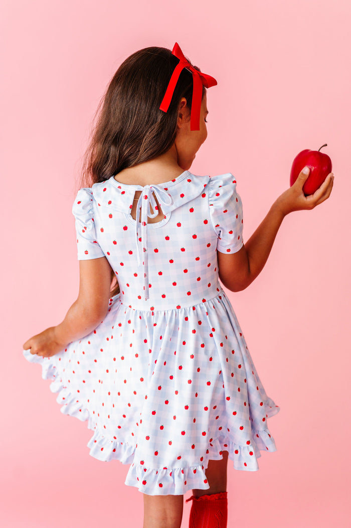 girl wearing light blue and white back to school dress with bow tie on back and red apples