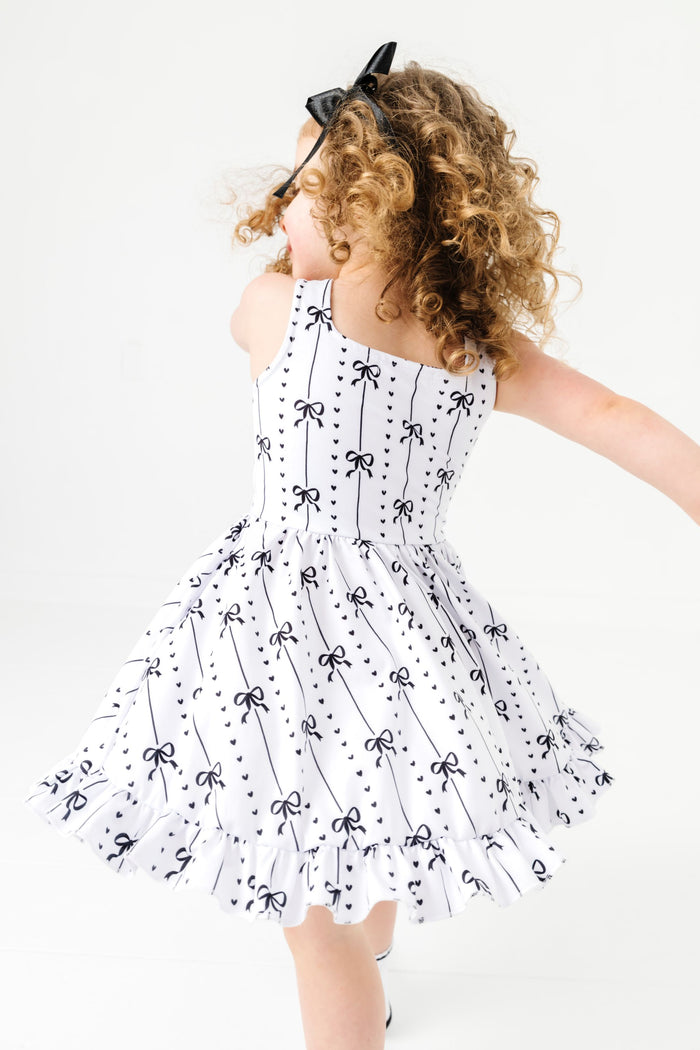 little girl twirling in white tank twirl dress with black bow pattern and matching sparkle black ribbon hair bow