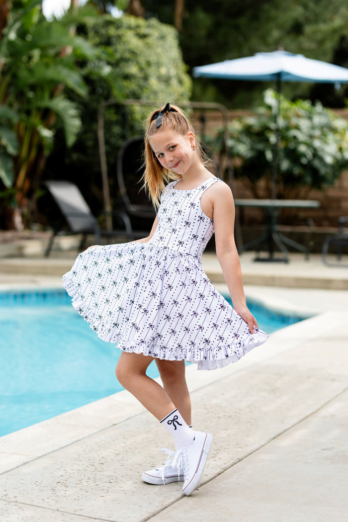 little girl poolside in white sleeveless twirl dress with black bow design paired with black sparkle hair bow and white crew socks with black bow design to match