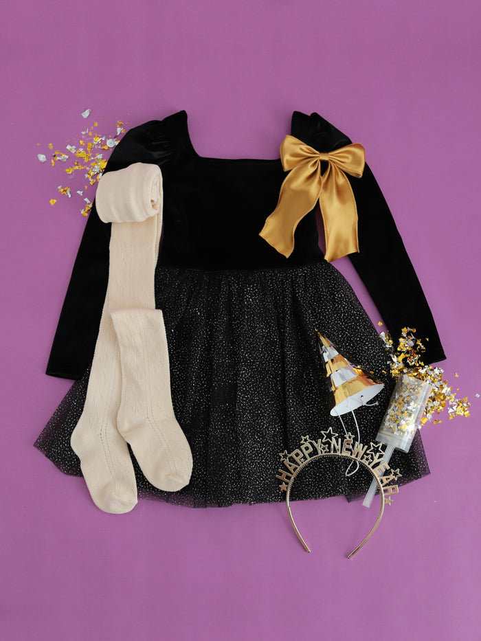flatlay of girls new years eve party outfit of black velvet and gold sparkle tutu dress and matching vanilla fancy tights and gold satin double bow