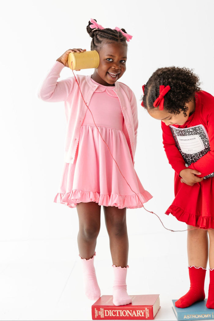 little girl standing on book in solid pink bow to toe matching dresses cardigans and accesories standing beside girl in red school outfit
