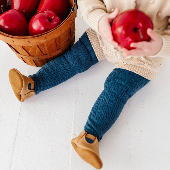 baby girl holding apple in blue cable knit tights paired with cream sweater set