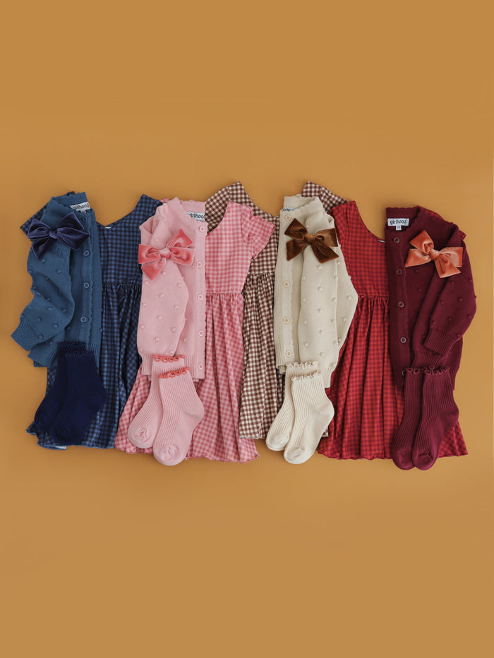 flat lay of four fall gingham twirl dresses and matching cardigans, velvet bows and midi socks