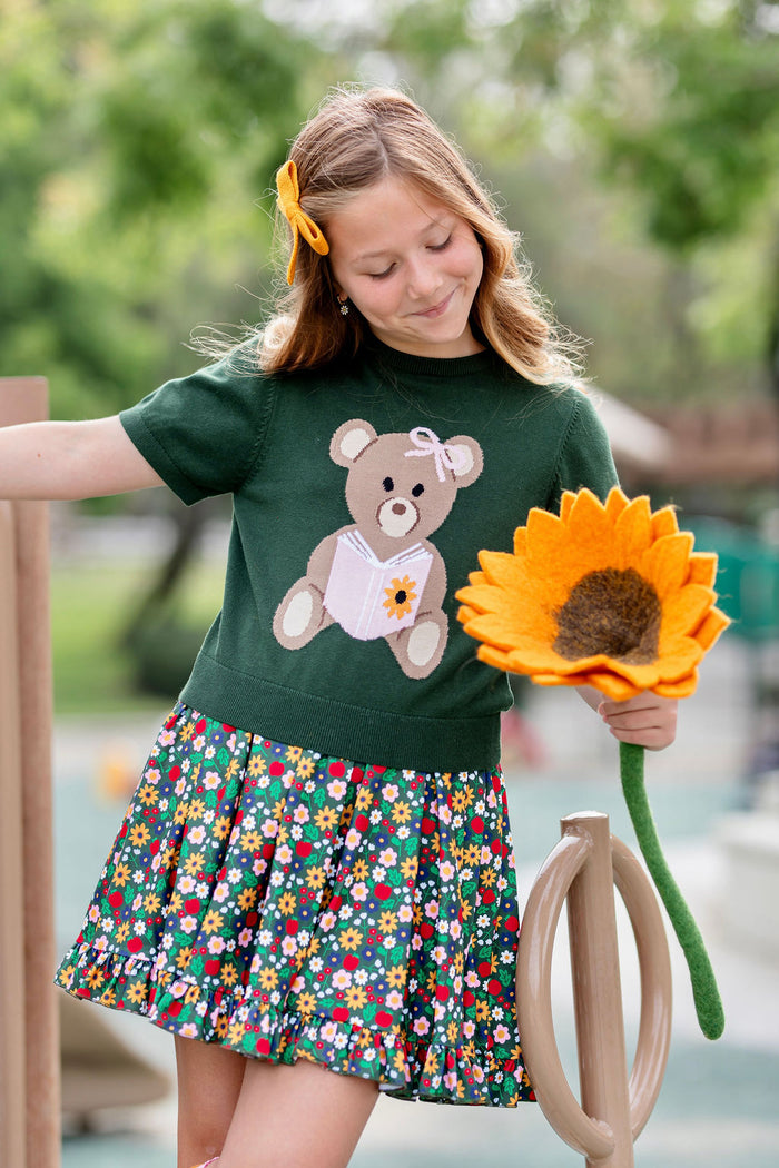 girl holding sunflower in short sleeve green sweater top with bear design and forest green floral and apple print twirl dress