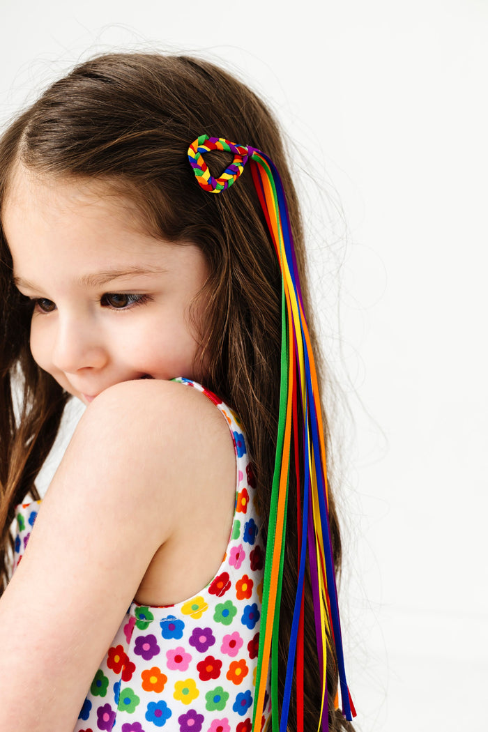 little girl wearing rainbow floral sleeveless twirl dress paired with braided heart clip with rainbow ribbon streamers