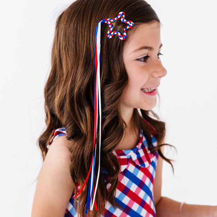 Girl wearing a red, white, and blue hair bow with a checkered dress on a white background