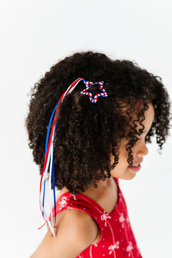 little girl wearing braided ribbon star clip with red, white and blue streamers to match 4th of July dress