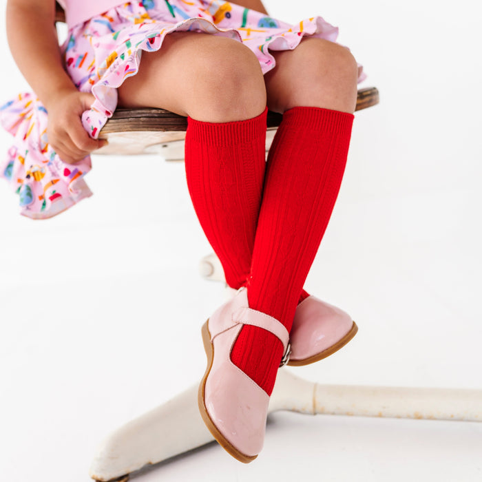 little girl sitting at desk in bright red cable knit knee socks paired with pink back to school themed twirl dress and pink mary janes
