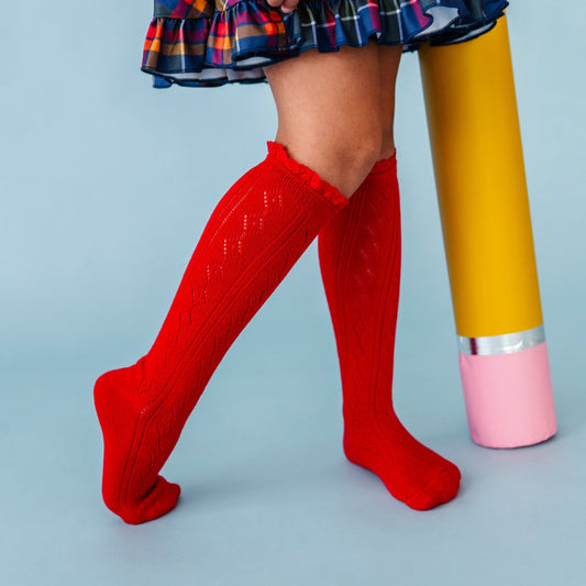 girl holding giant pencil prop in bright red pointelle lace top knee socks and navy plaid school dress