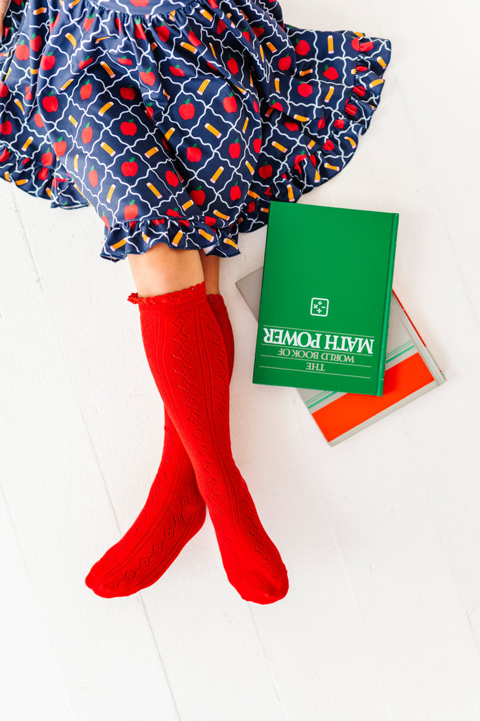 girl with textbooks in bright red pointelle knee socks with lace trim paired with navy blue apple and pencil print school dress