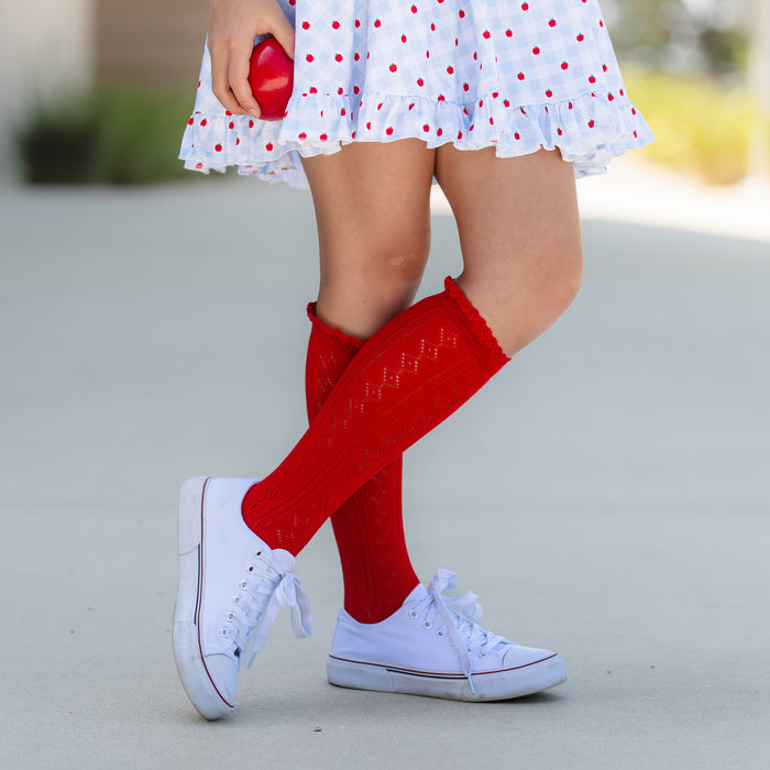 girl wearing blue and white apple print gingham twirl dress paired with bright red pointelle knee socks and holding an apple