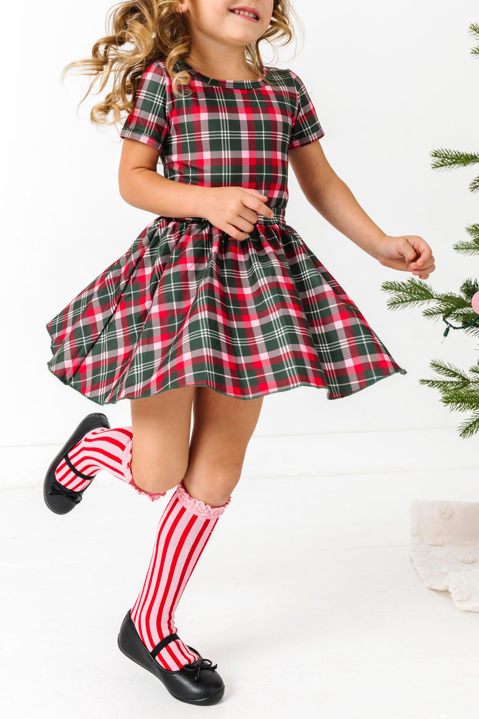 girl twirling in classic Christmas plaid top and skirt paired with pink and red striped knee high socks with lace trim
