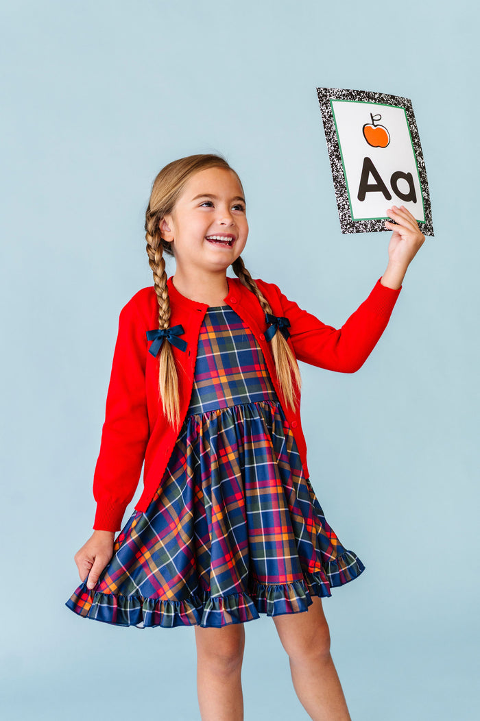 girl holding apple alphabet cart in navy plaid twirl dress paired with bright red cotton knit cardigan for school