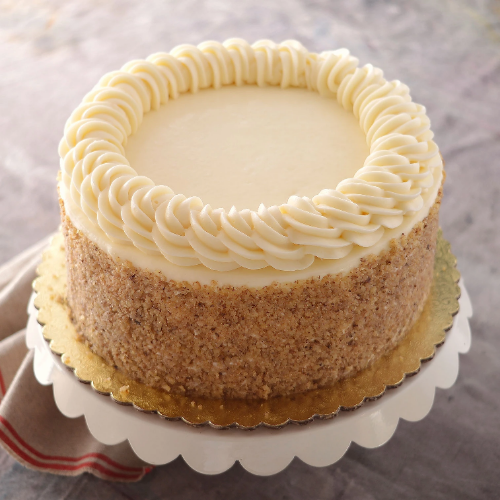 Round cake with white frosting, rosettes, nut-covered sides, on a white stand with gold cake board.