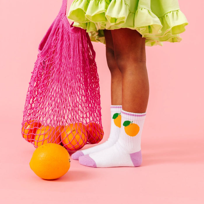 little girl holding bag of oranges in orange themed crew socks from three pack paired with lime green summer twirl dress