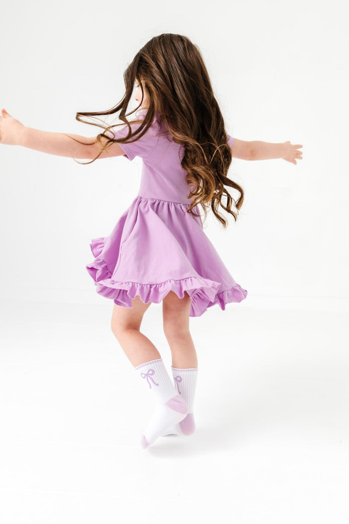 little girl twirling in solid lavender twirl dress with matching white crew socks featuring lavender bow design