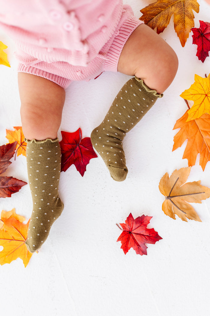 baby girl sitting in autumn leaves wearing pink sweater wet paired with olive green and ivory dot lettuce trim knee socks