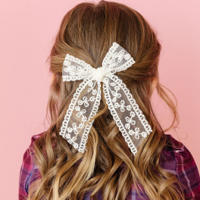 Girl wearing a plaid dress with a large lace hair bow on a pink background
