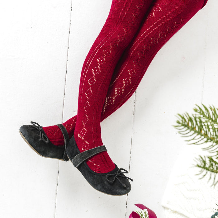 closeup of girl by Christmas tree in open knit crimson red tights and black mary janes