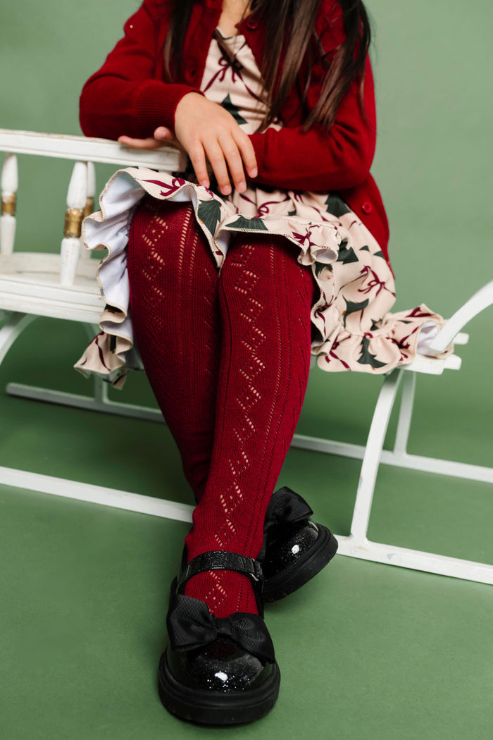 girl sitting on sled in crimson crochet tights to match vintage Christmas tree outfit