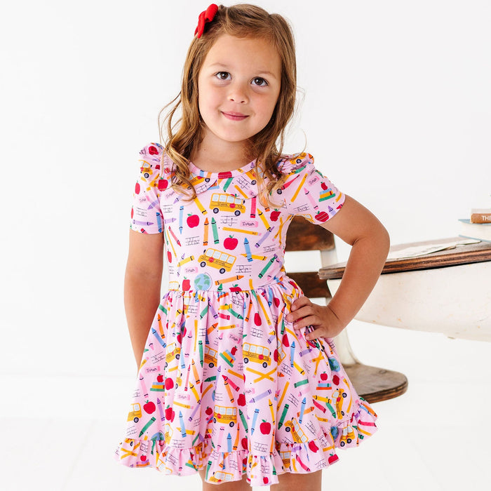 Girl wearing pink back to school dress with school buses, pencils, crayons and apples