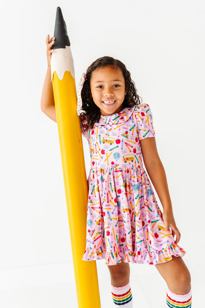 girl wearing pink first day of school themed print dress with rainbow striped knee high socks