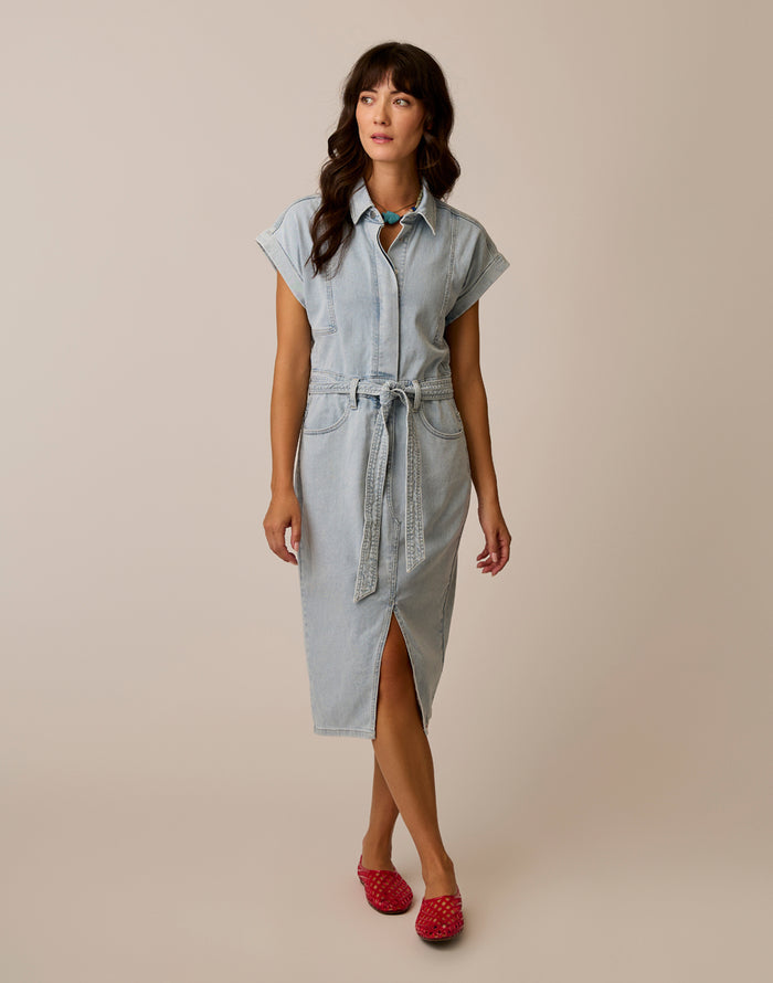 Woman wearing a light blue denim dress with a belt on a beige background