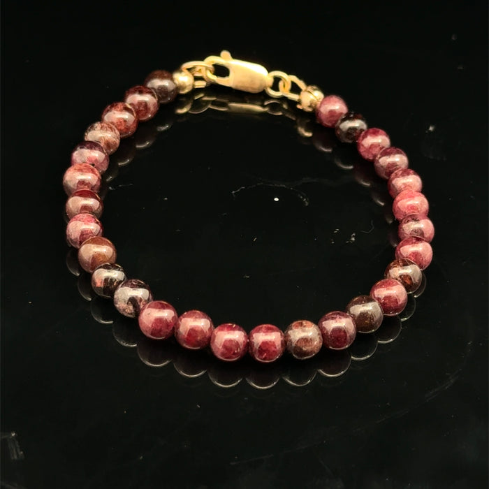 Red garnet gemstone beaded bracelet with a gold-filled lobster claw on a black background, front overview.