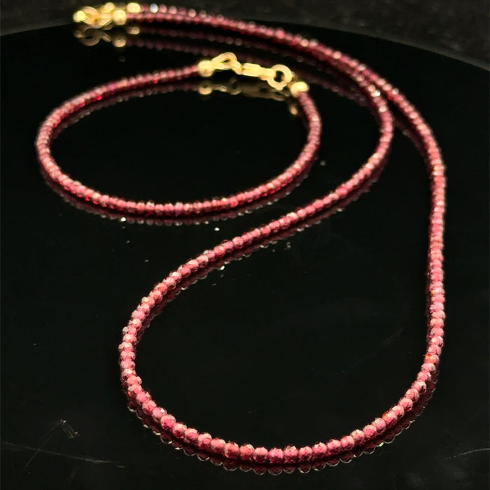 Red garnet gemstone beaded bracelet with its matching necklace and a gold-filled lobster claw on a black background, front overview.