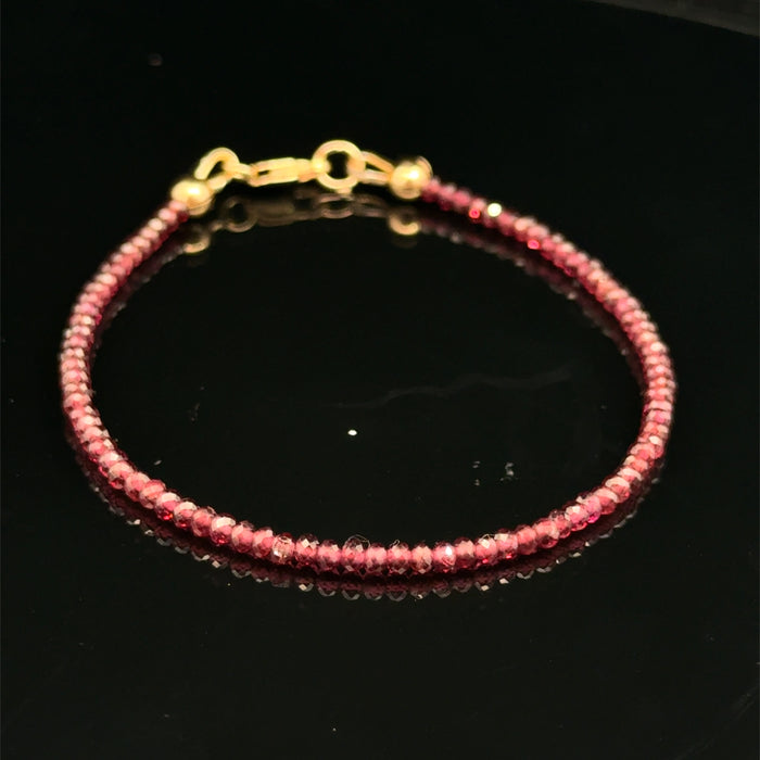 A 2mm faceted roundel red garnet gemstone beaded bracelet with a gold-filled lobster claw on a black background, front overview.