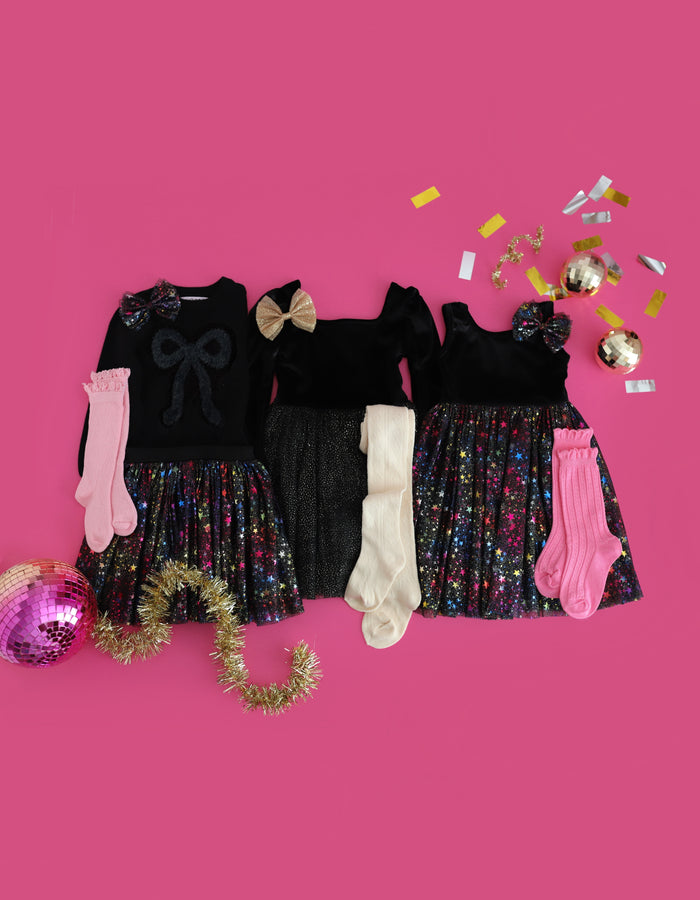 flatlay of three New Years Eve outfits for girls featuring black velvets, sparkly tulle and foil stars with matching bows and stockings