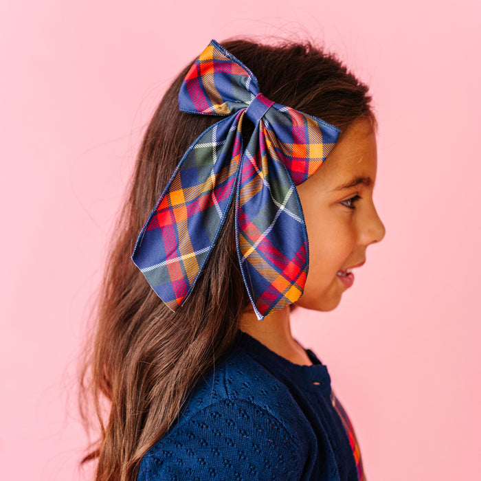 girl wearing navy plaid dress and matching fabric print bow on clip paired with pointelle navy blue cardigan